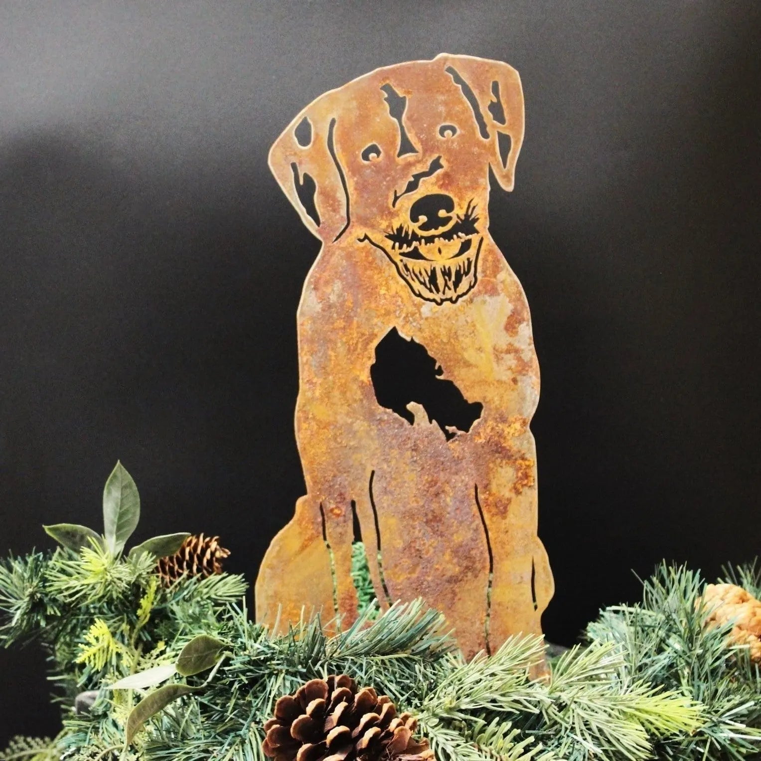 Rusty metal silhouette of a Wirehaired Pointing Griffon, surrounded by pine and pinecones against a black backdrop.