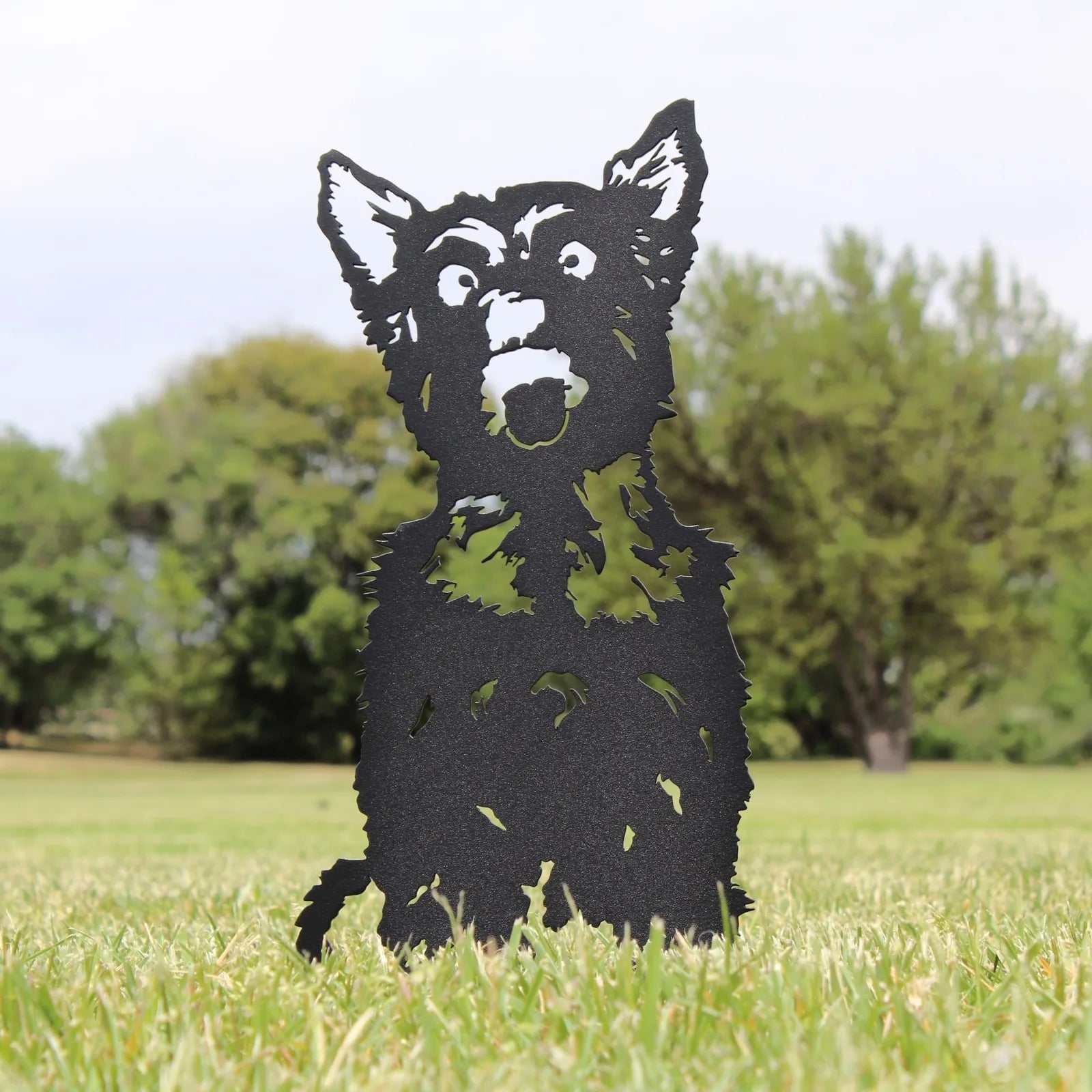 Black metal silhouette of a Yorkshire Terrier in a grassy outdoor setting, showcasing intricate detailing and design.