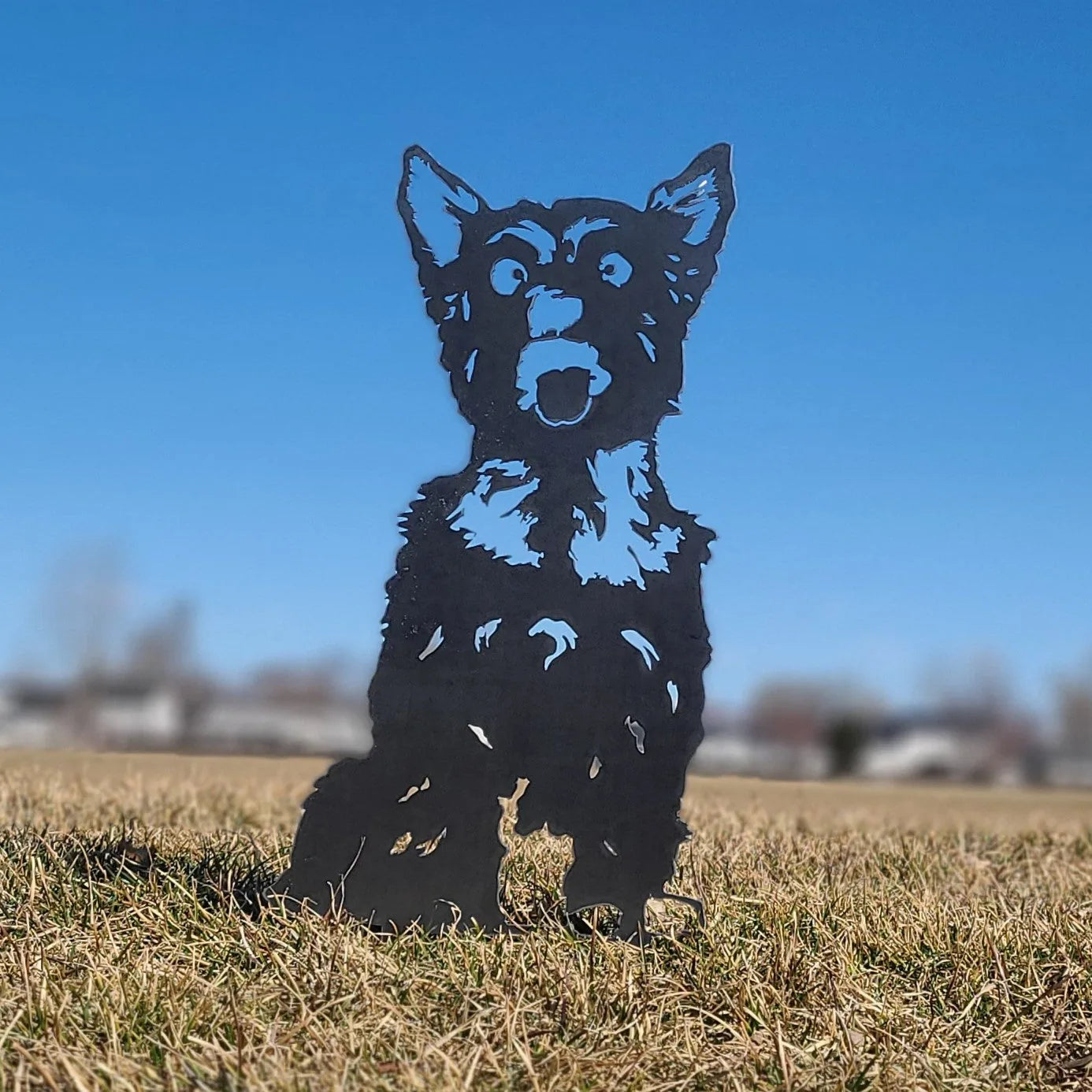 Black metal silhouette of a Yorkshire Terrier standing in grass against a clear blue sky, perfect for outdoor decor.