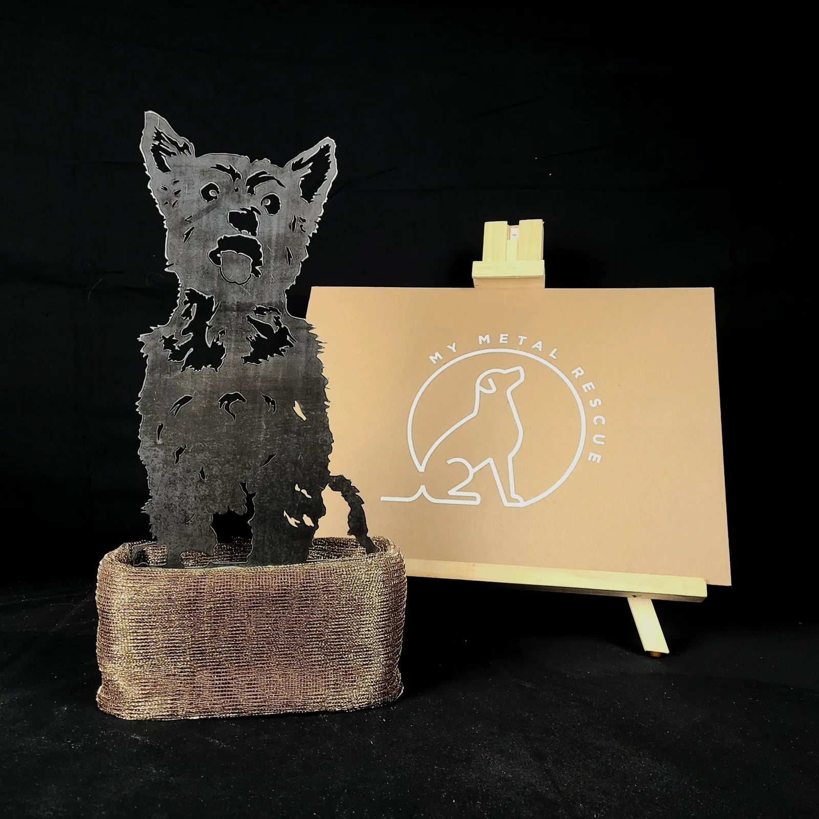 Handmade metal silhouette of a Yorkshire Terrier in weathering steel, displayed on a woven base against a black backdrop.